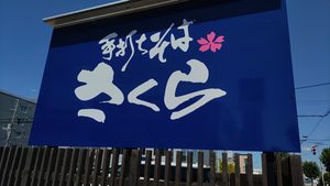 青い板に白文字で「手打ちそば さくら」と書かれた大きな看板。