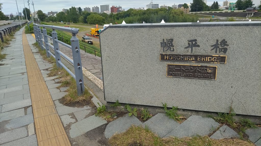 幌平橋の橋名板。HOROHIRA BRIDGEとPORTLAND SQUAREの文字があり、近くに会場へ降りる階段がある