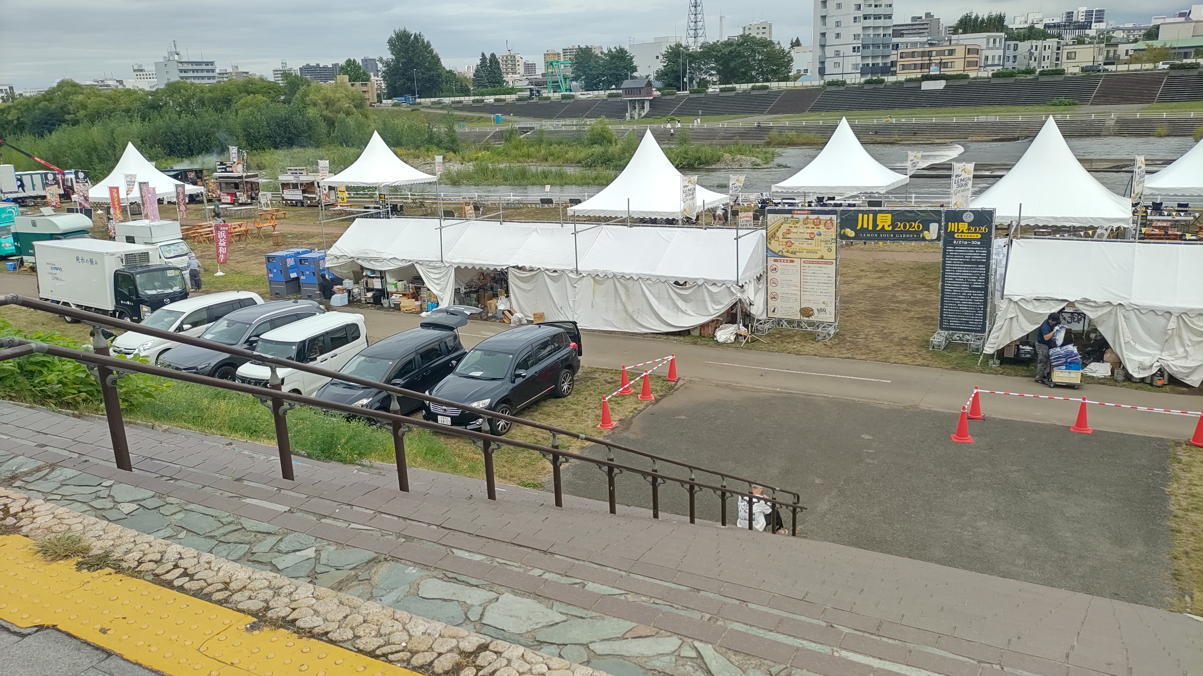 幌平橋の上から見た川見2026の会場。河川敷に白いテントや会場ゲートが並んでいる