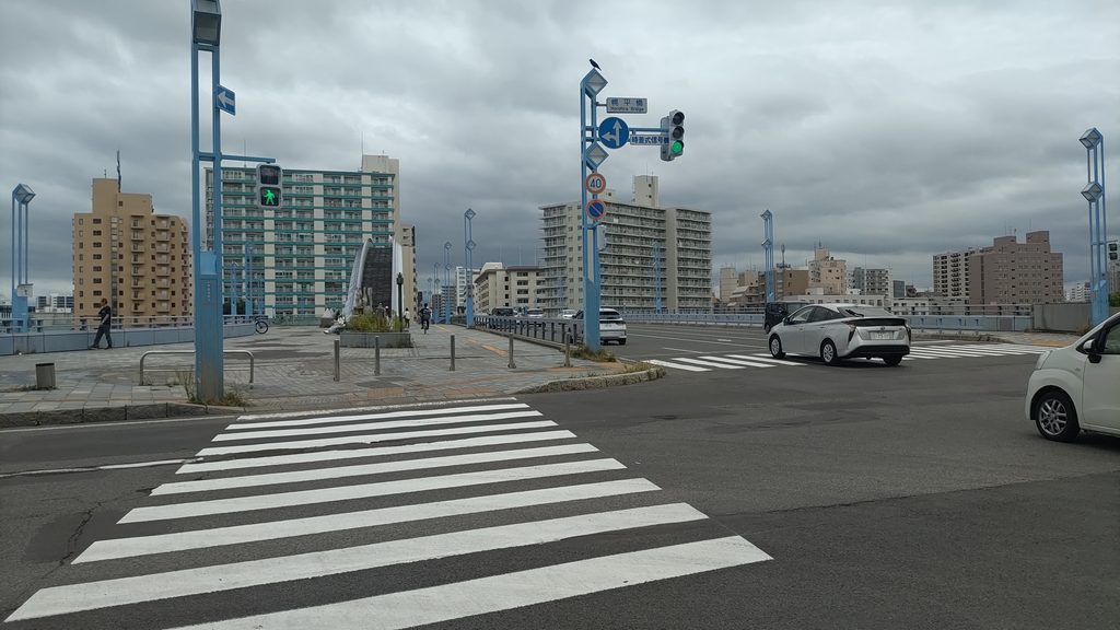 幌平橋手前の交差点。横断歩道と橋へ続く歩道、幌平橋方向の標識が見える
