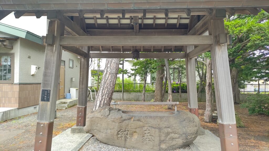 丘珠神社境内にある石造りの手水鉢と木造の手水舎