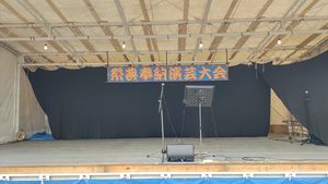 「祭典奉納演芸大会」の看板が掲げられ、マイクと譜面台が設置されたステージ