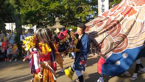丘珠神社の境内で、金色の衣装を着た3人の獅子取りが大きな獅子の前で舞う様子