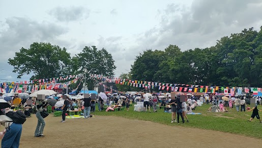 国旗の飾りの下に屋台と傘を差した来場者が並ぶ美香保夏まつり会場