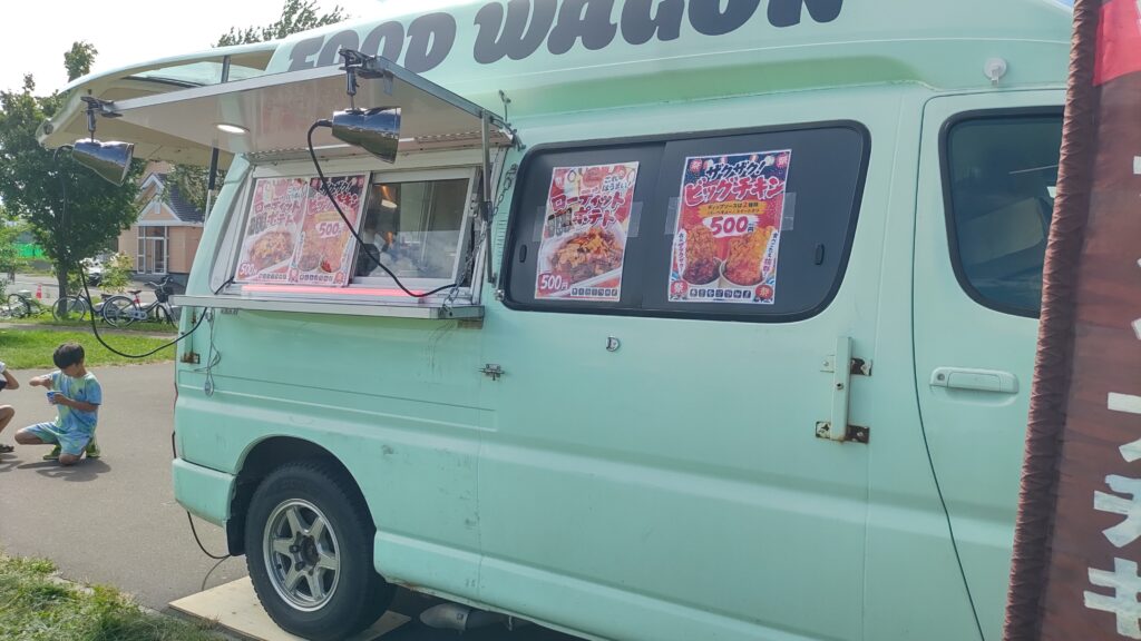 チキンやポテトのメニューを掲示した緑色のキッチンカー