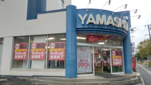 YAMASHITAの看板がある紳士服の山下 新道東店の入口と、周囲に掲示された完全閉店の案内