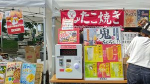 たこ焼きやチュロス、サワーなどを販売する露店に設置された10秒ピッタリチャレンジの機械とメニュー看板