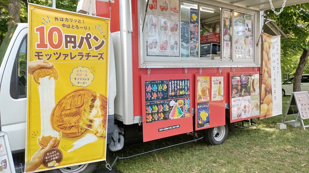 モッツァレラチーズ入り10円パンの大きな看板があるキッチンカー。かき氷やドリンクのメニューも掲示されている