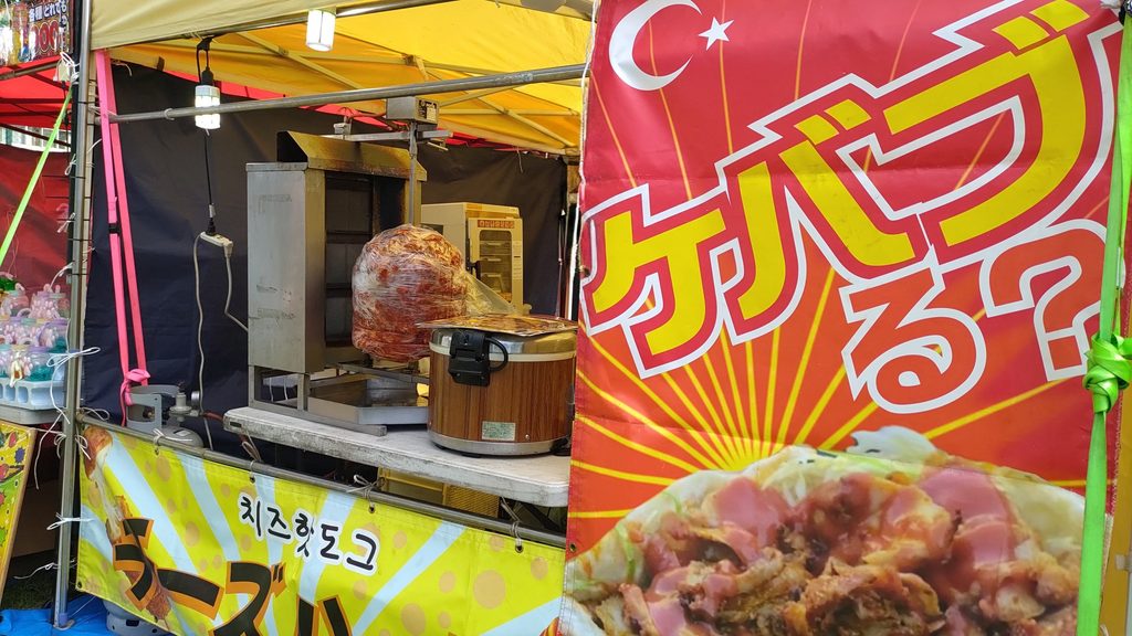 大きなケバブの看板と肉を焼く機械があるケバブの露店