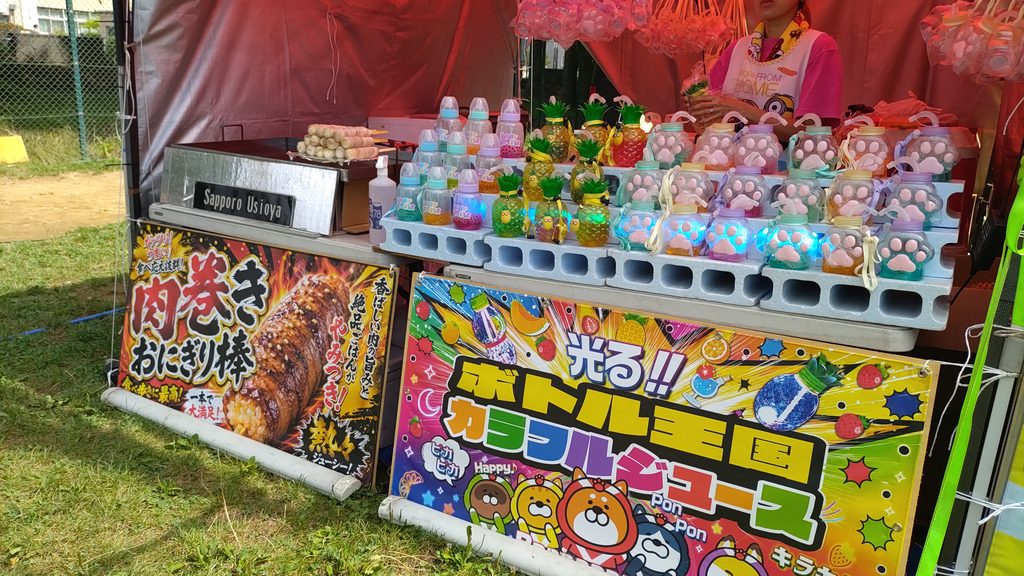 肉巻きおにぎり棒と、カラフルに光るボトル入りドリンクが並ぶ露店