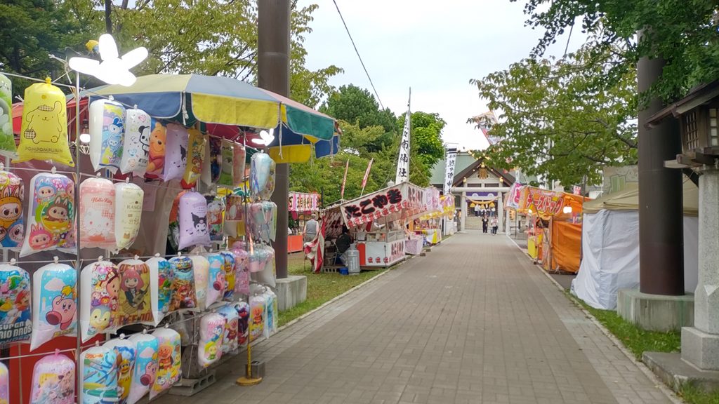 烈々布神社の参道に並ぶ例祭の露店と奥に見える本殿