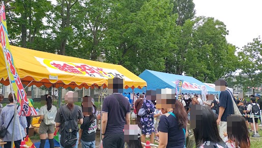 輪投げやヨーヨーなどの子ども向けコーナー前で順番を待つ親子連れ