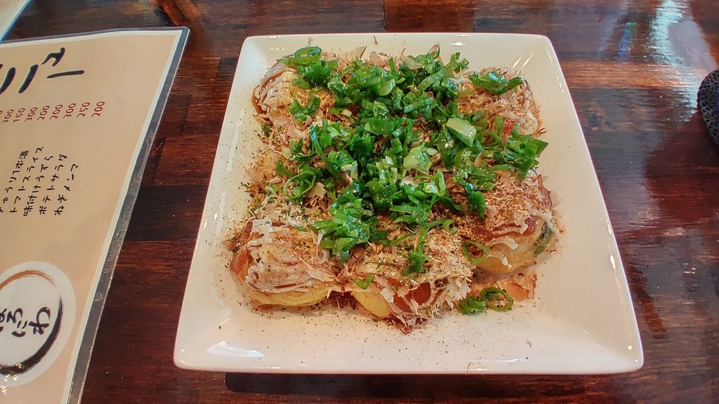 ぽろにわのねぎマヨたこ焼き。白い四角い皿に盛り付けられたたこ焼きに、刻んだ青ねぎやかつお節、ソースとマヨネーズがかかっている。